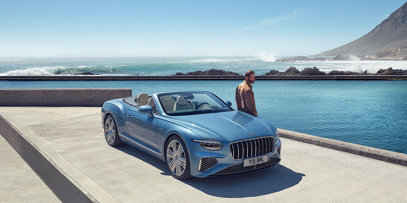 Bentley Hyderabad New Bentley Continental GTC Azure convertible front view in Light Windsor blue paint with 22 inch ten spoke wheels parked by the sea in the sunshine
