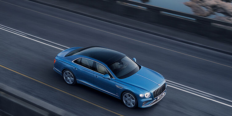 Bentley Hyderabad New Bentley Flying Spur Azure sedan in Light windsor blue paint by Mulliner, with 22 inch Azure wheels seen from overhead driving dynamically on a country road